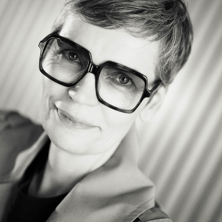 Frau mit kurzen Haaren und großer Brille, lächelnd in schwarz-weiß porträtiert.