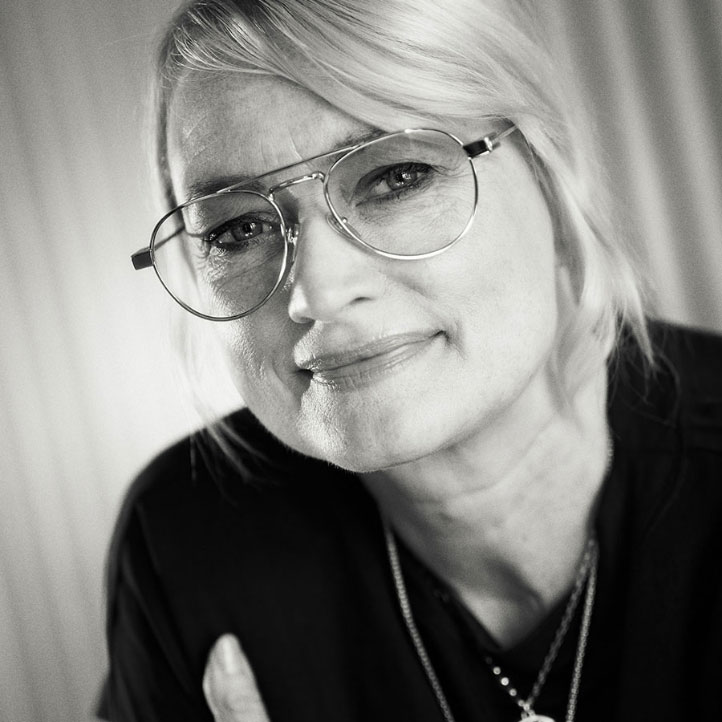 Frau mit Brille lächelt leicht, schwarz-weiß Porträt, Kopf nach rechts geneigt, Haare hinter dem Ohr.