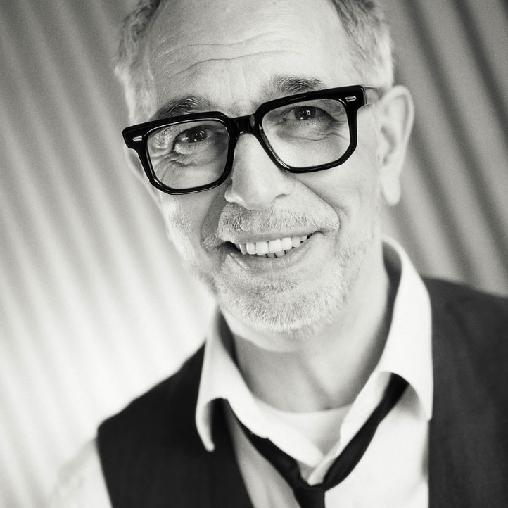 Ein lächelnder älterer Mann mit Brille, Hemd und Weste, Blick zur Kamera. Schwarz-weiß Fotografie, Hintergrund unscharf.