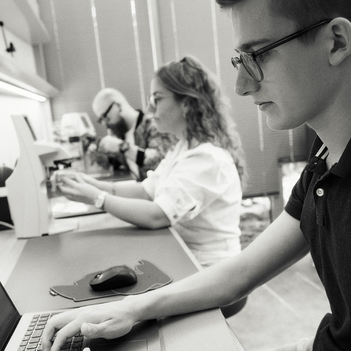 Drei Personen arbeiten konzentriert an Computern und Mikroskopen in einem Labor.